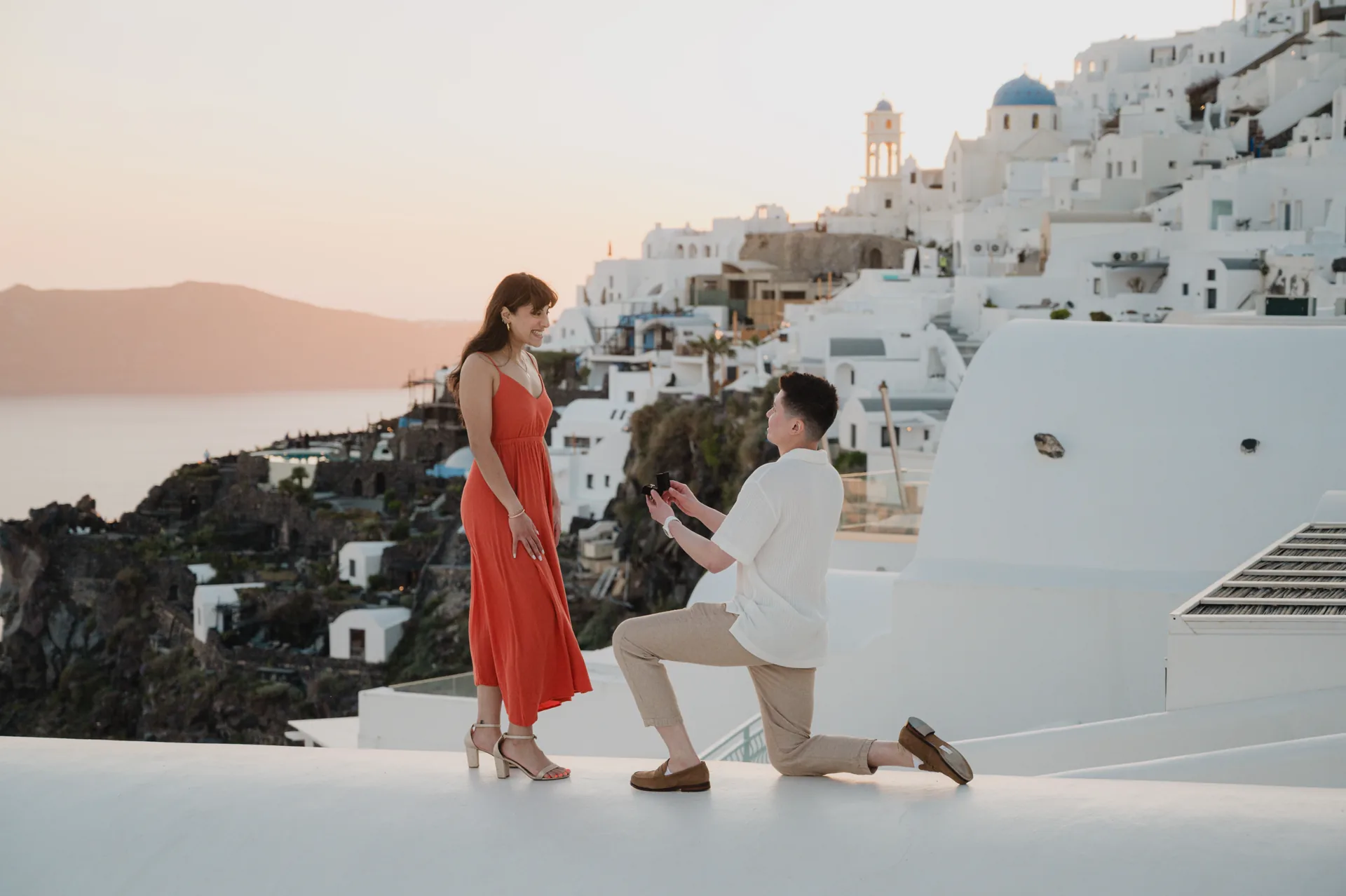 Erin smiling as Fredrik kneels with an open ring box at sunset